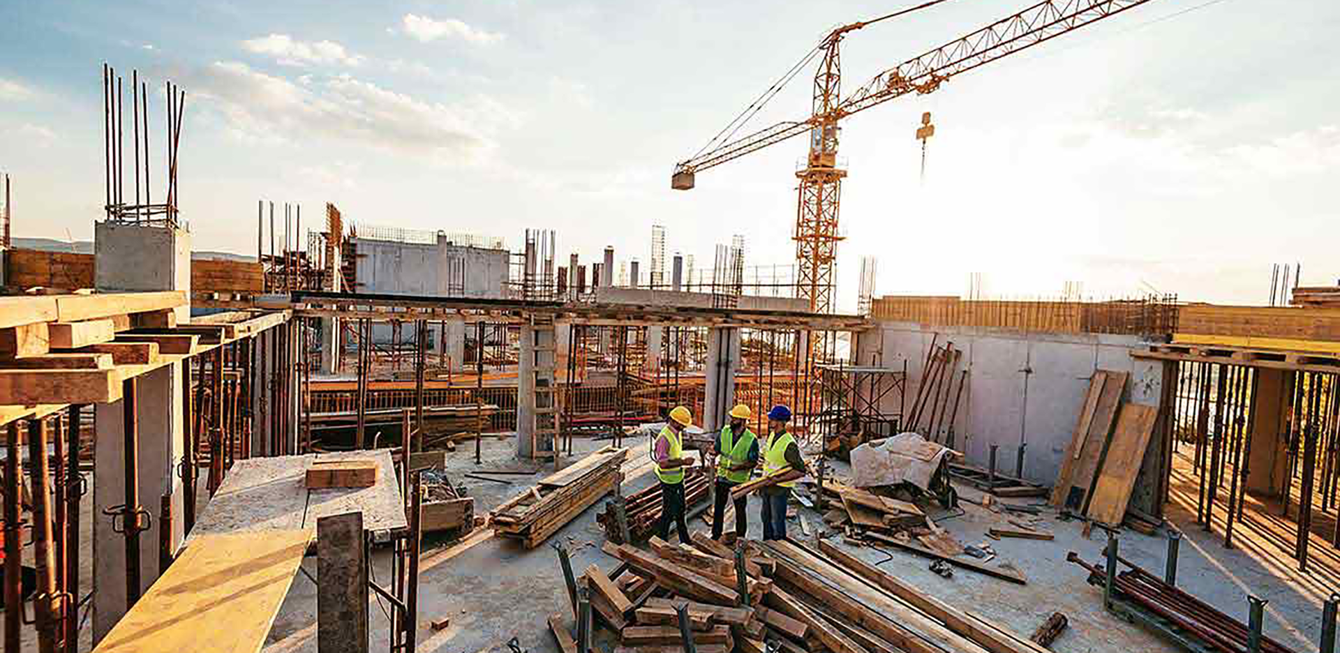 A trio of construction workers standing on a rooftop that's under construction.