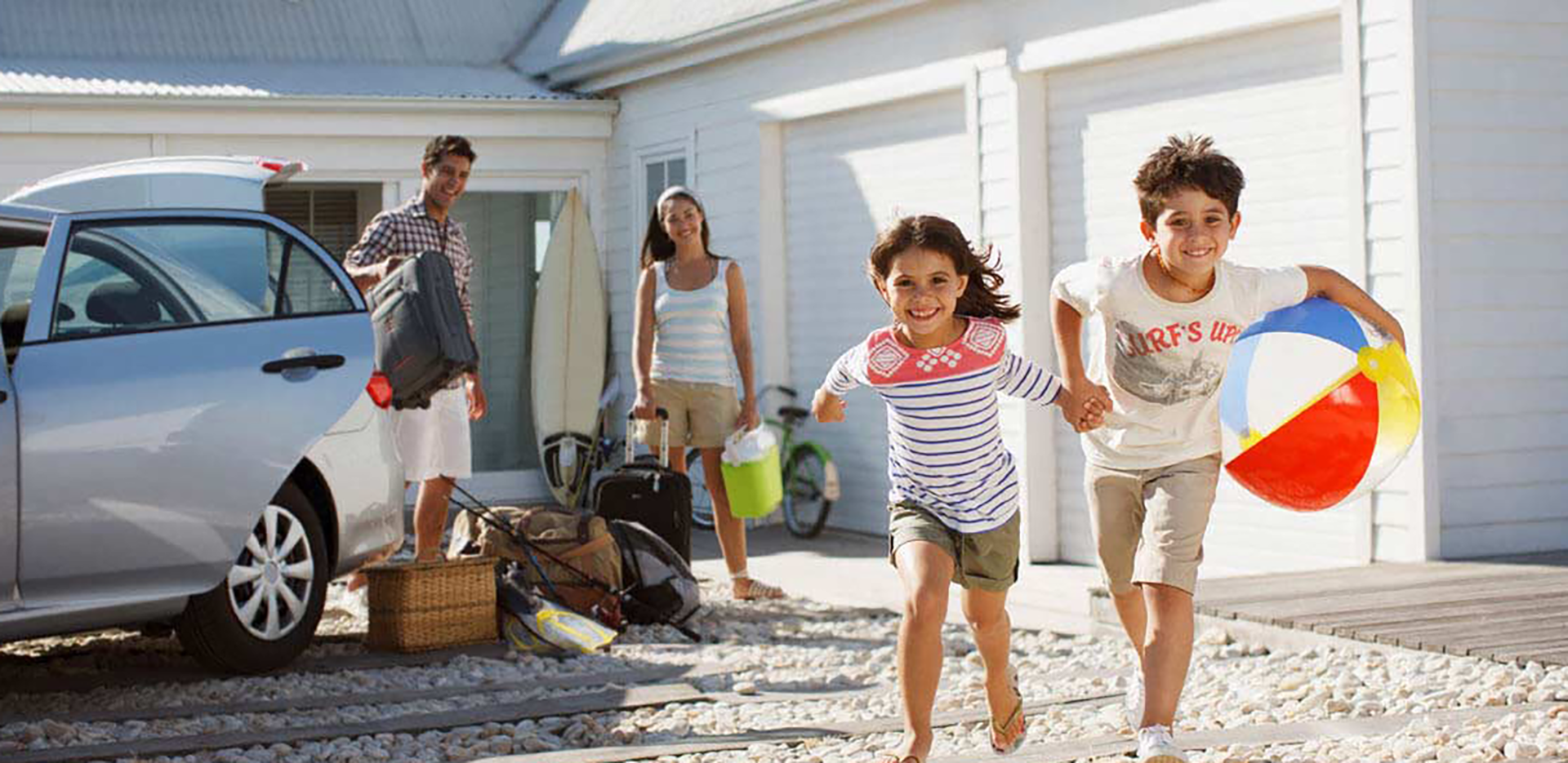 A family packing vacation supplies into a car in front of a rental home.