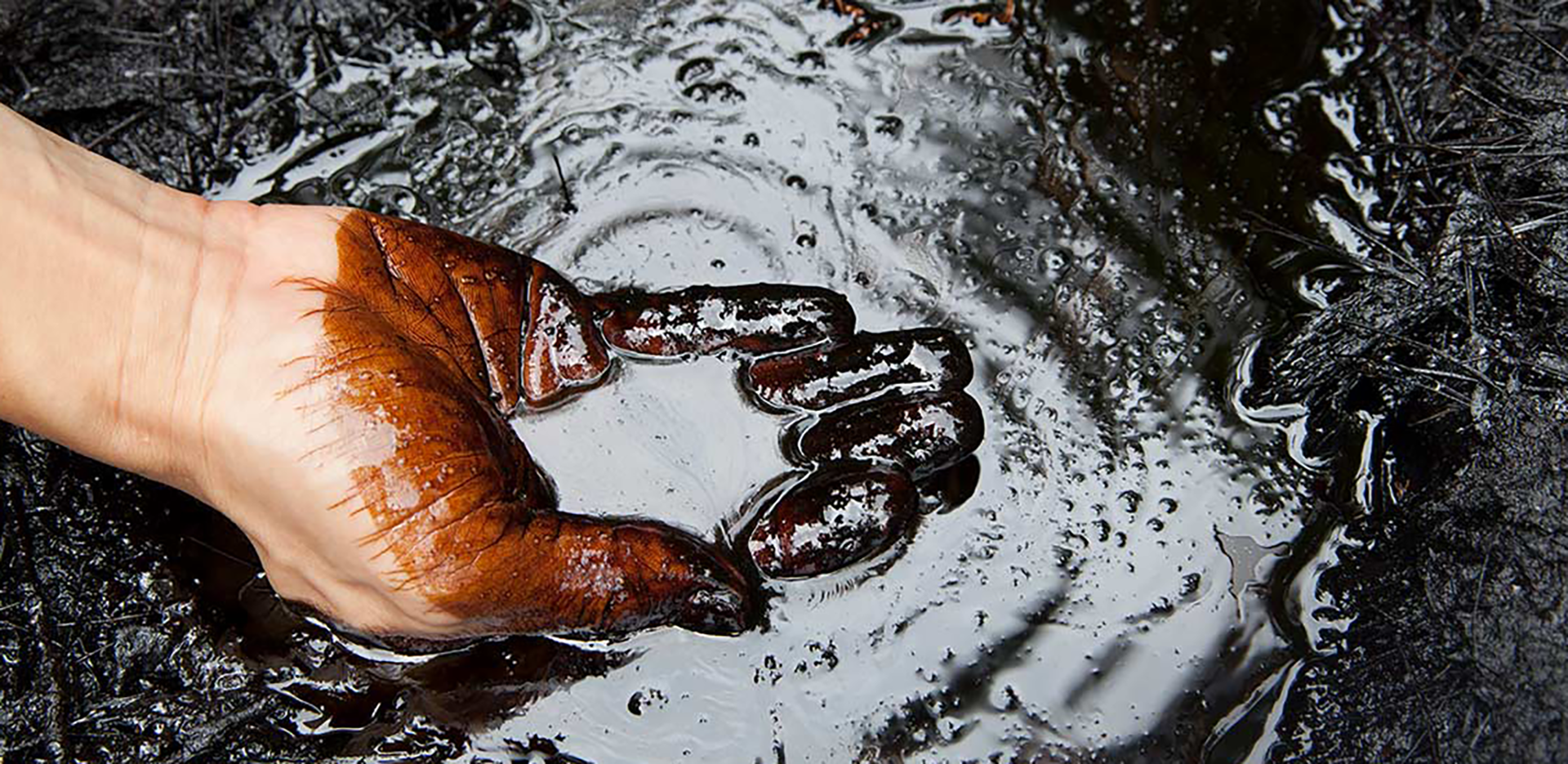 A hand scooping a handful of oil off the ground.
