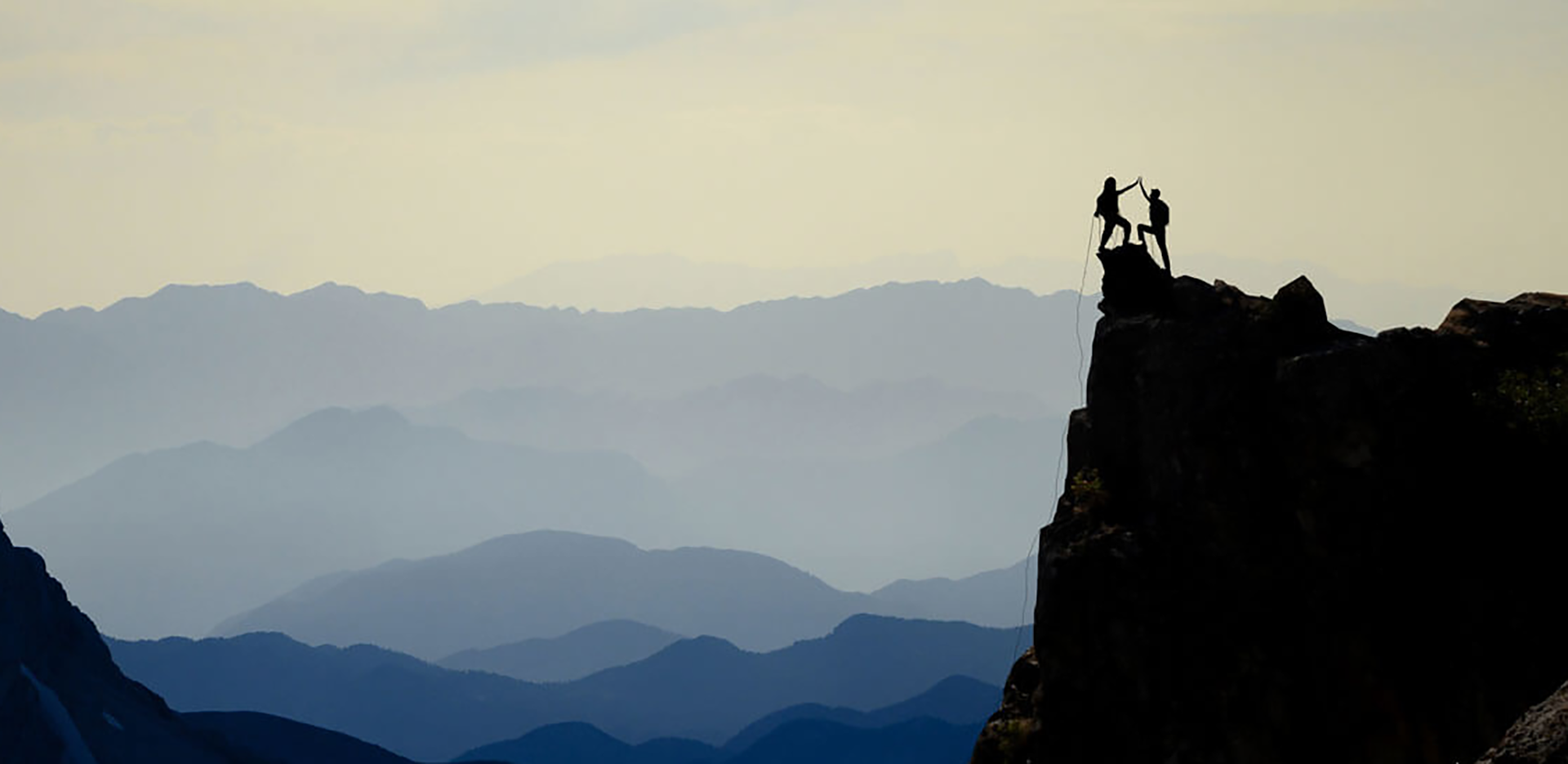 A pair of climbers in silhouette high-fiving at the top of a cliff.