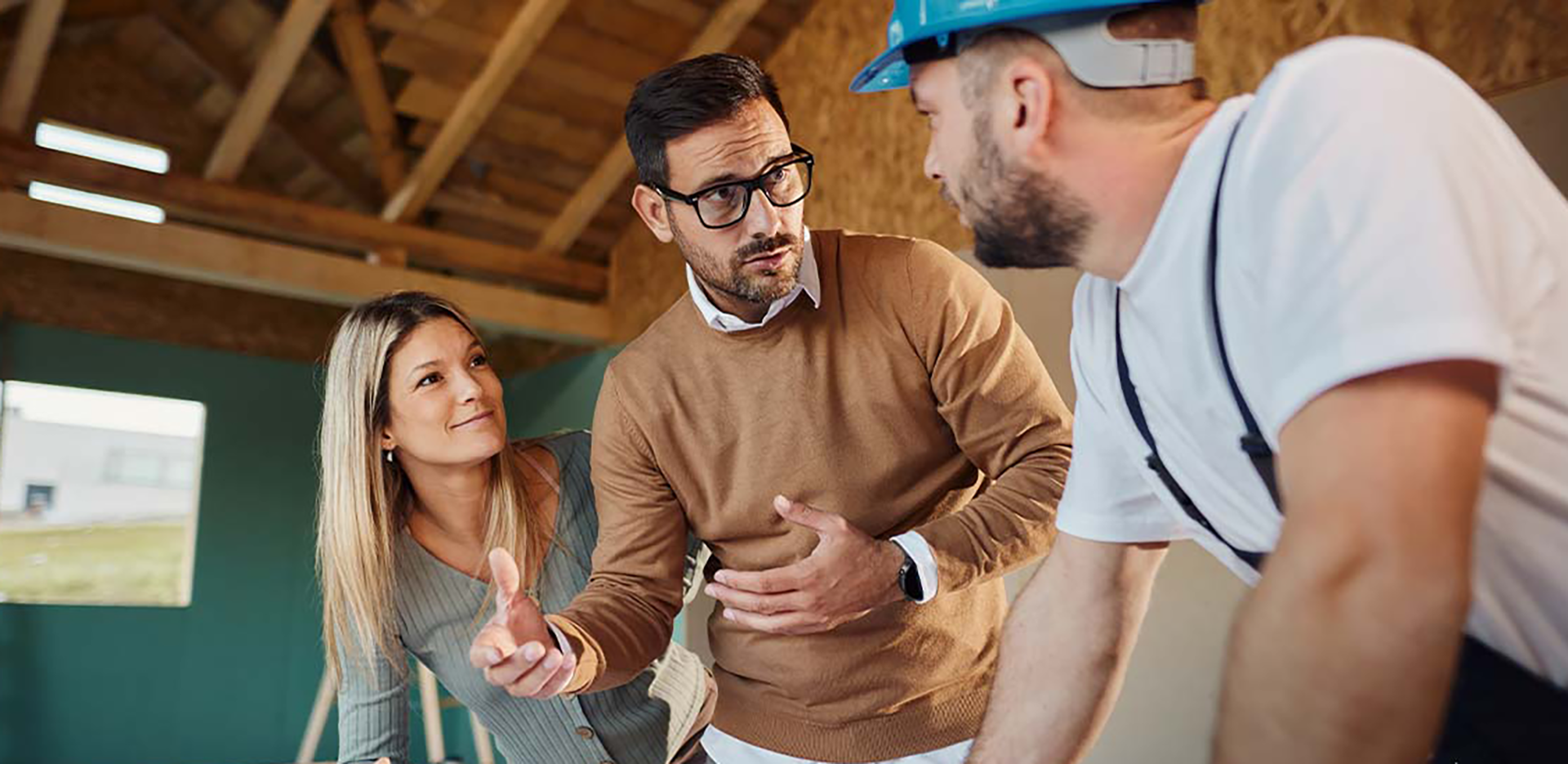 Two people speak with a contractor in a house that's under construction.