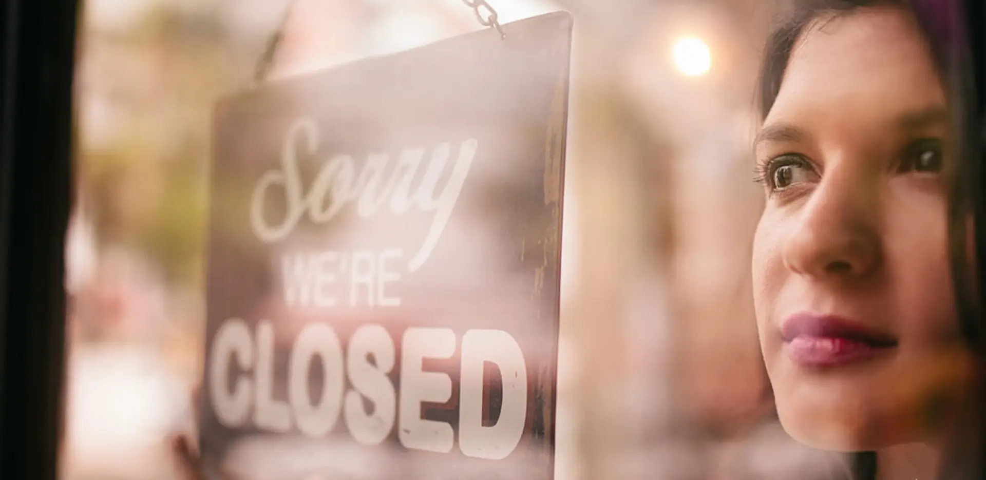 A close up of a woman hanging a 'Sorry We're Closed' sign.
