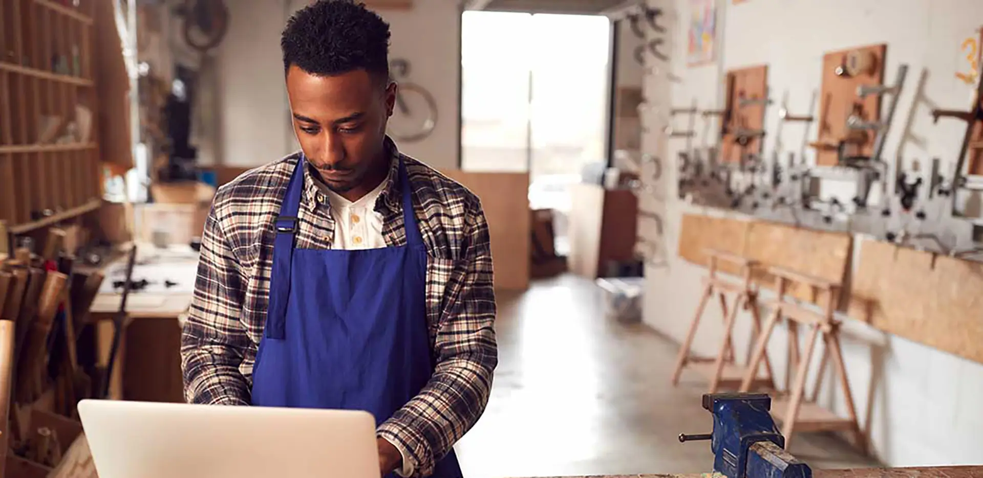 A man wearing an apron working on a laptop computer with construction equipment in the background.