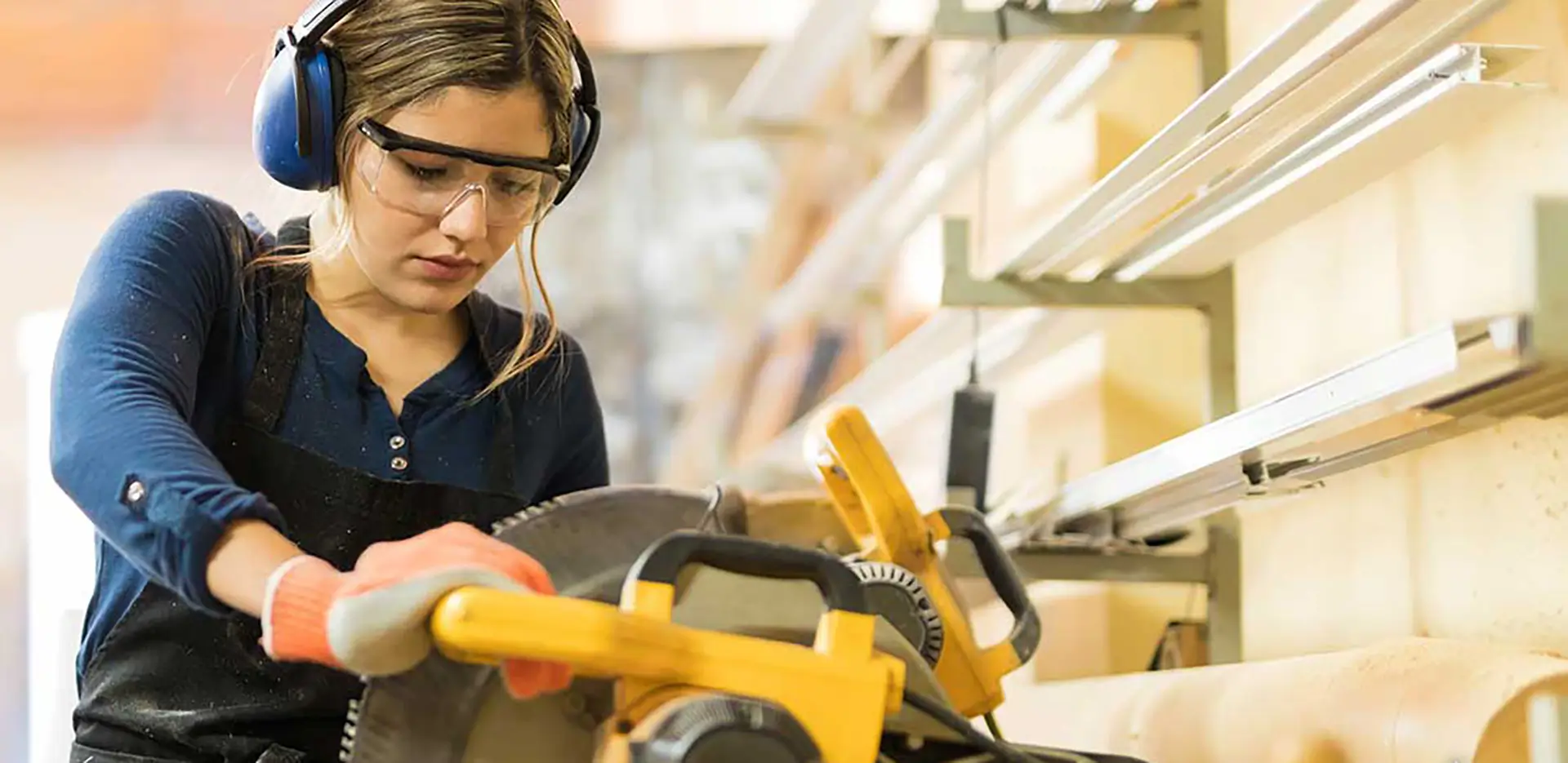 A woman wearing earmuffs operating a buzz saw.