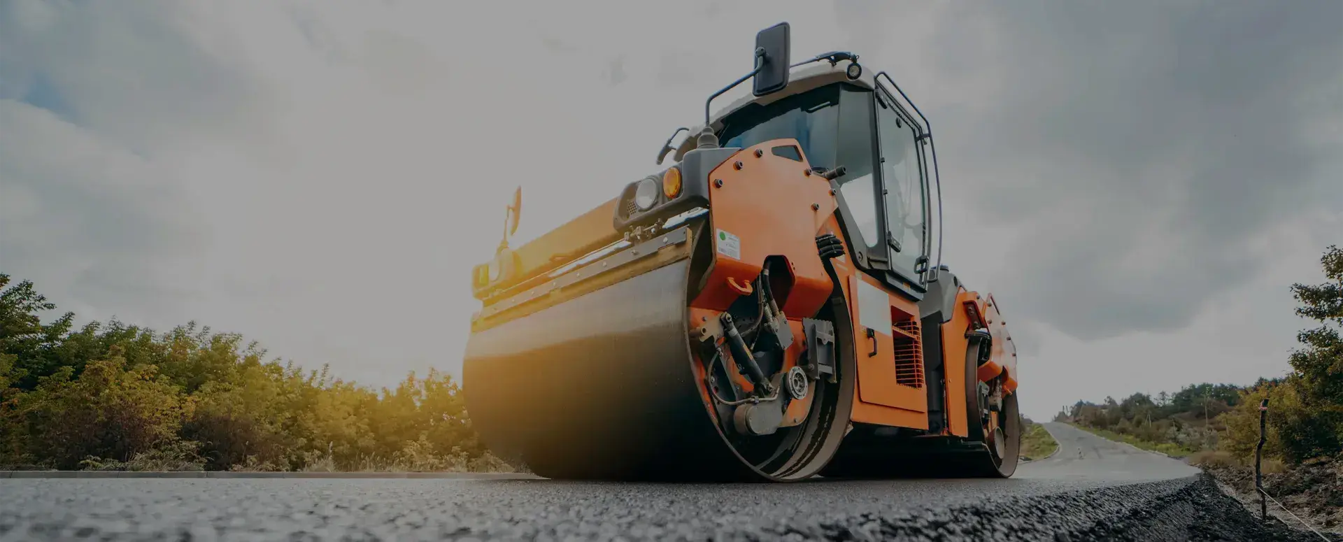 An orange asphalt compacting roller vehicle on a freshly paved road.