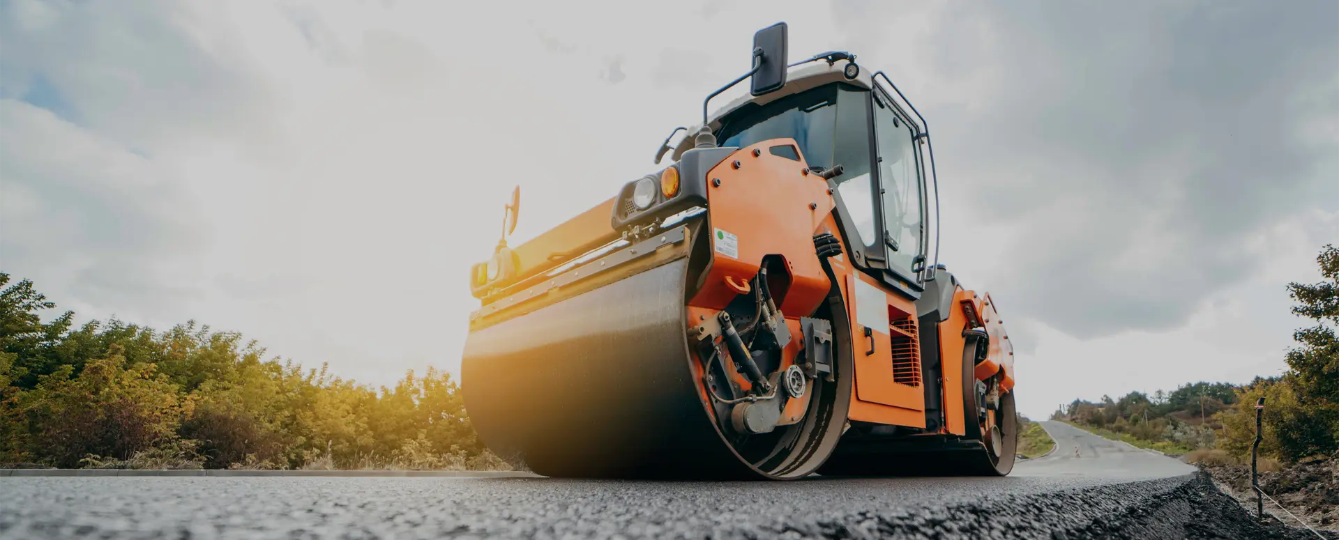 An orange asphalt compacting roller vehicle on a freshly paved road.