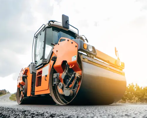 An orange asphalt compacting roller vehicle on a freshly paved road.