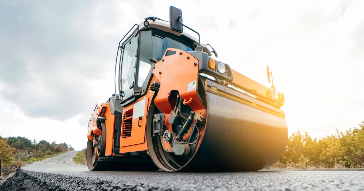An orange asphalt compacting roller vehicle on a freshly paved road.