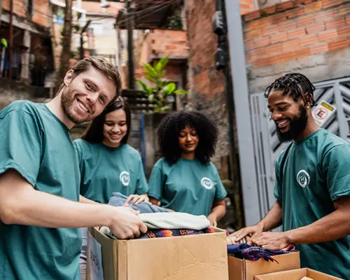 A group of people in identical t-shirts folding and placing clothes into boxes.
