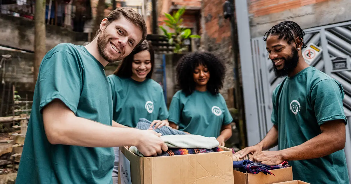 A group of people in identical t-shirts folding and placing clothes into boxes.