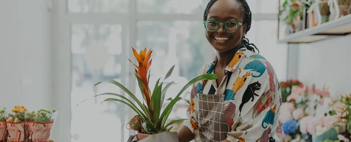A smiling woman standing in a flower shop holding a clipboard.