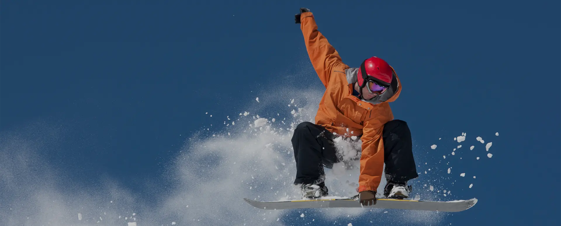 An airborne snowboarder grabbing his board and leaving behind a trail of snow in the air.