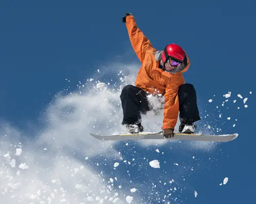 An airborne snowboarder grabbing his board and leaving behind a trail of snow in the air.