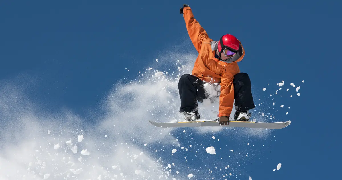An airborne snowboarder grabbing his board and leaving behind a trail of snow in the air.