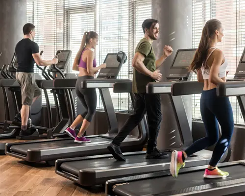 People running on treadmills at a gym with large windows along the wall.