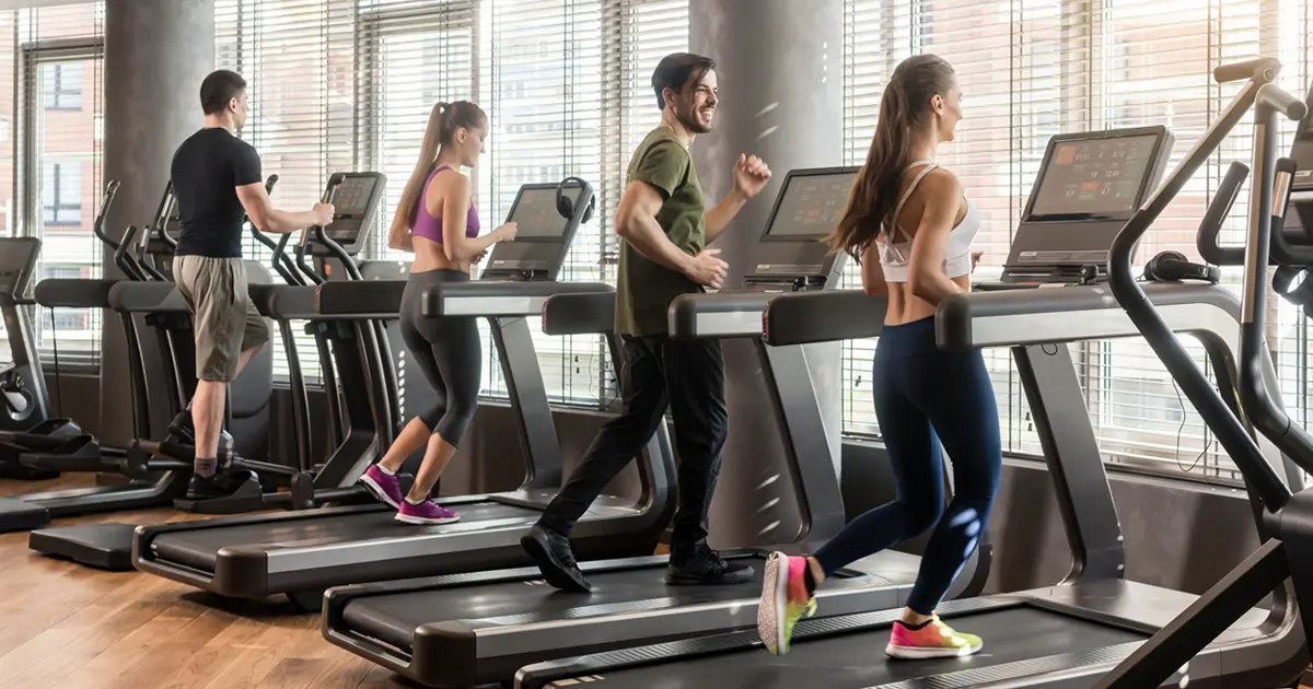 People running on treadmills at a gym with large windows along the wall.