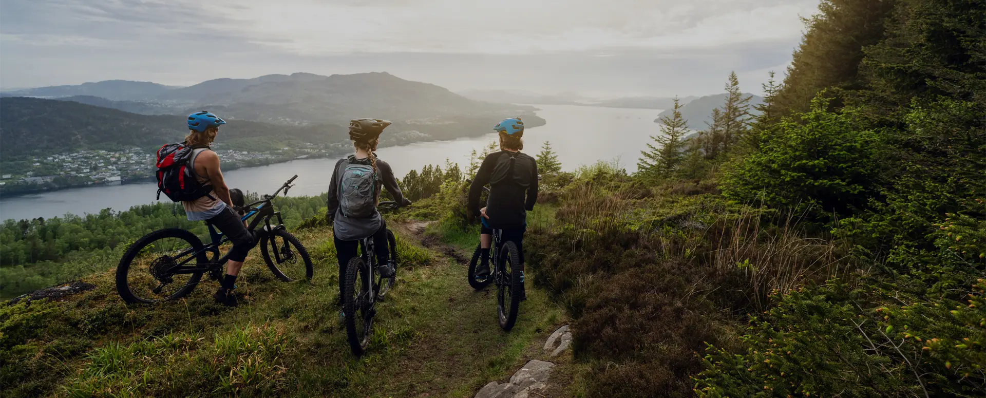A group of mountain bikers on a hilltop overlooking a lake and mountains.
