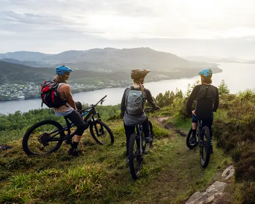 A group of mountain bikers on a hilltop overlooking a lake and mountains.