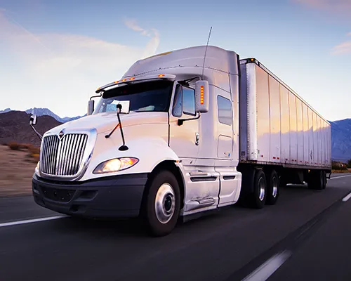 A white semi-truck driving along a desert road with mountains in the distance.