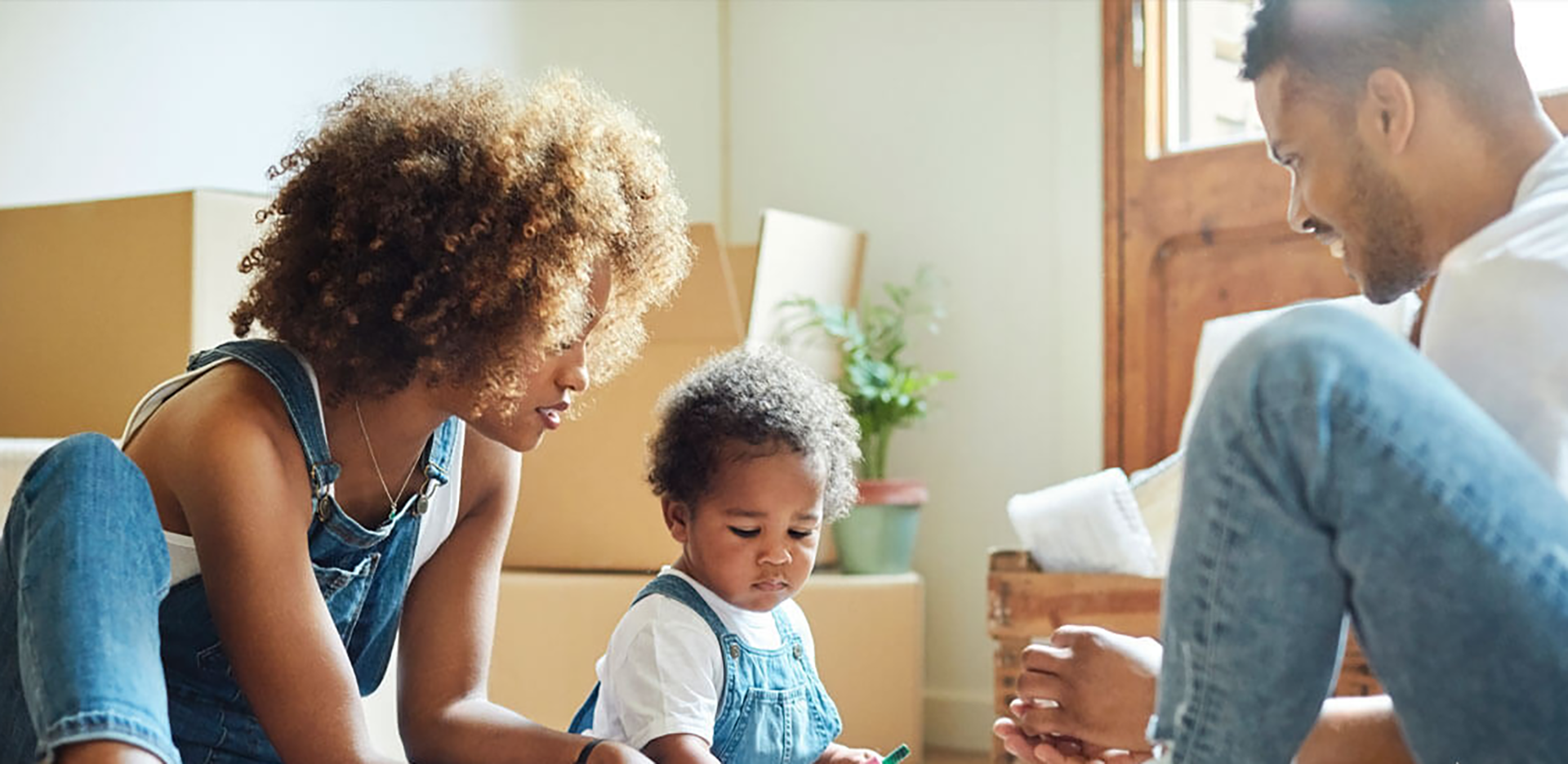 Parents sitting with their young toddler in front of moving boxes.