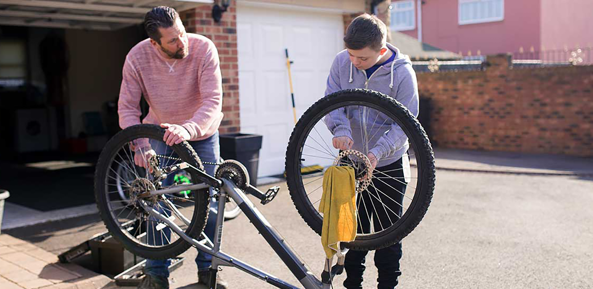 A father and son working on repairing a bicycle in their driveway.