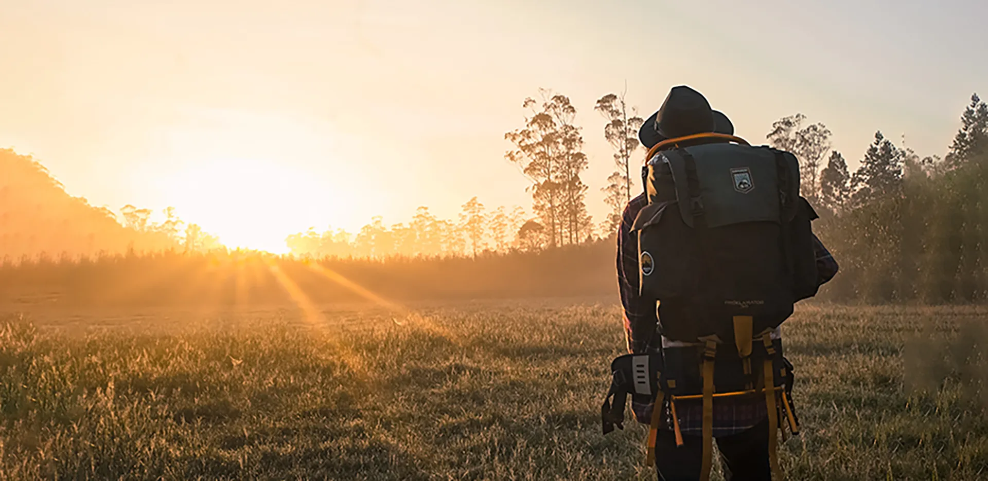 A person wearing a backpacking backpack looking at the sunset.