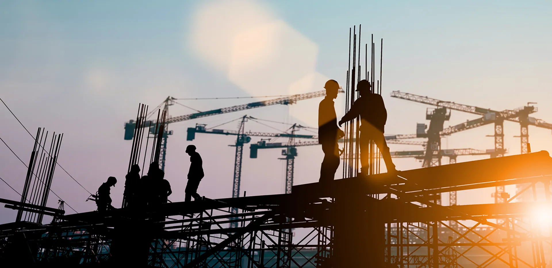 Silhouettes of a group of construction workers with cranes in the background.