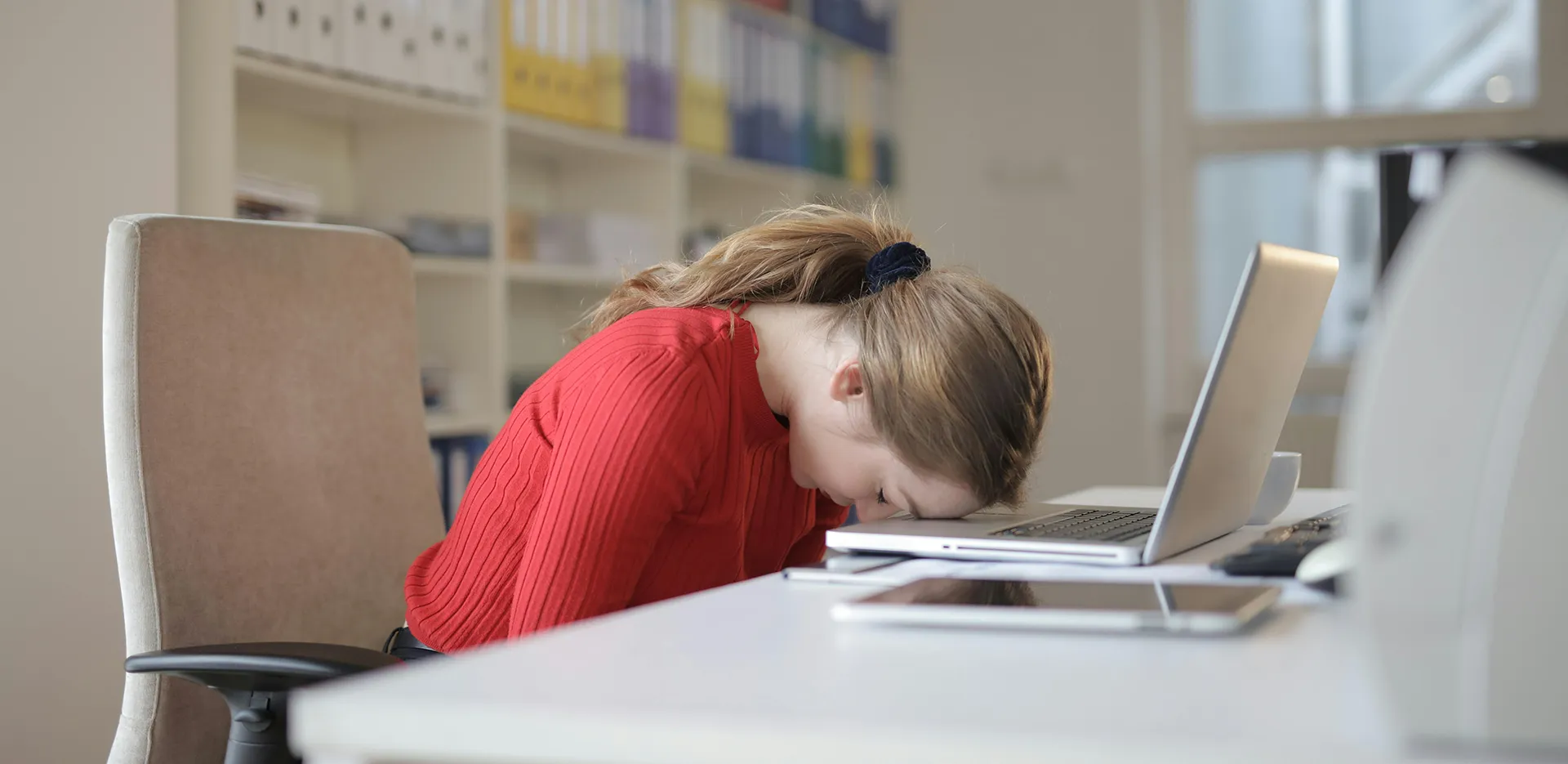 A woman resting her forehead on her laptop keyboard.