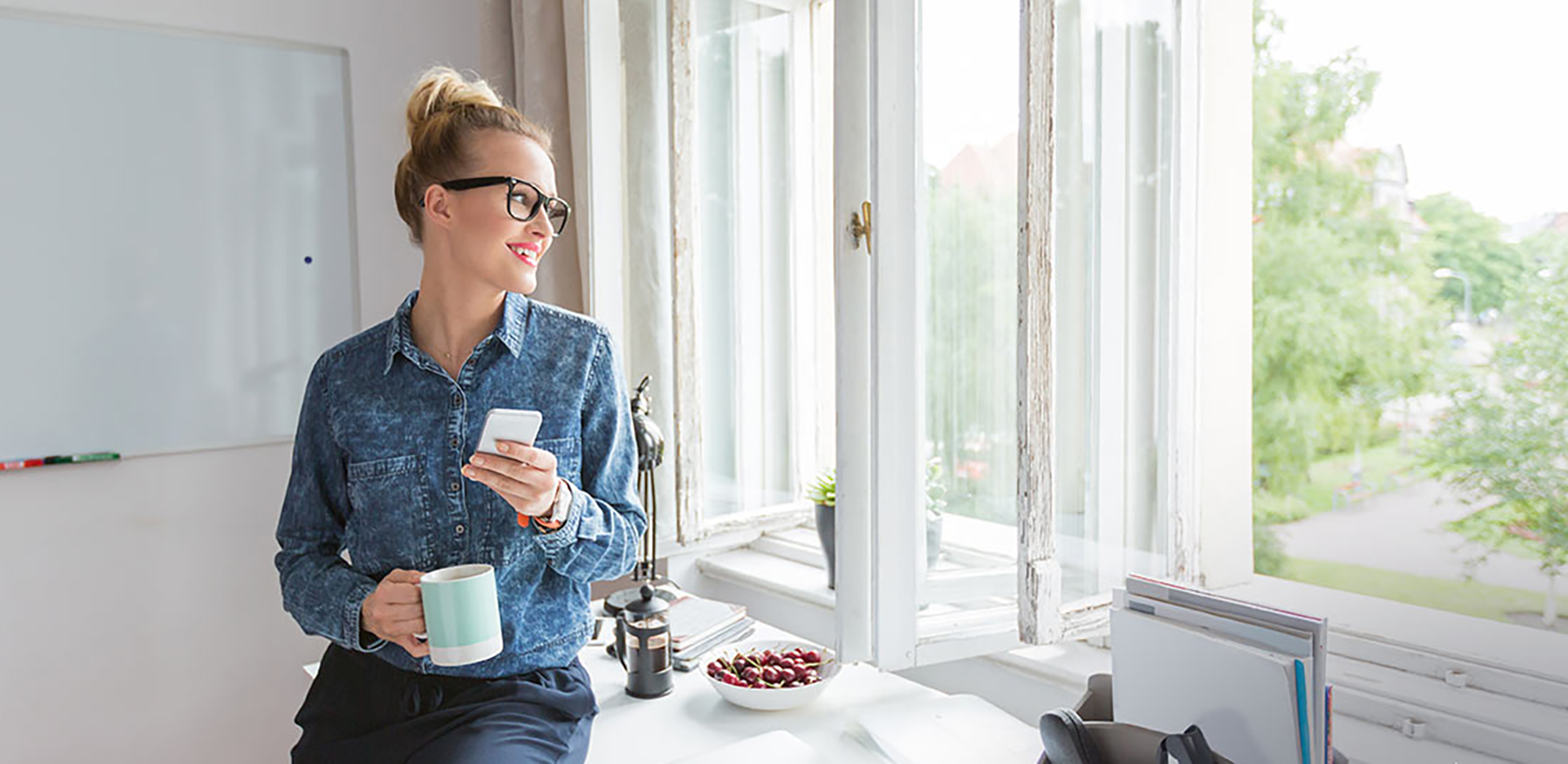 A woman holding her cell phone and looking out the window.