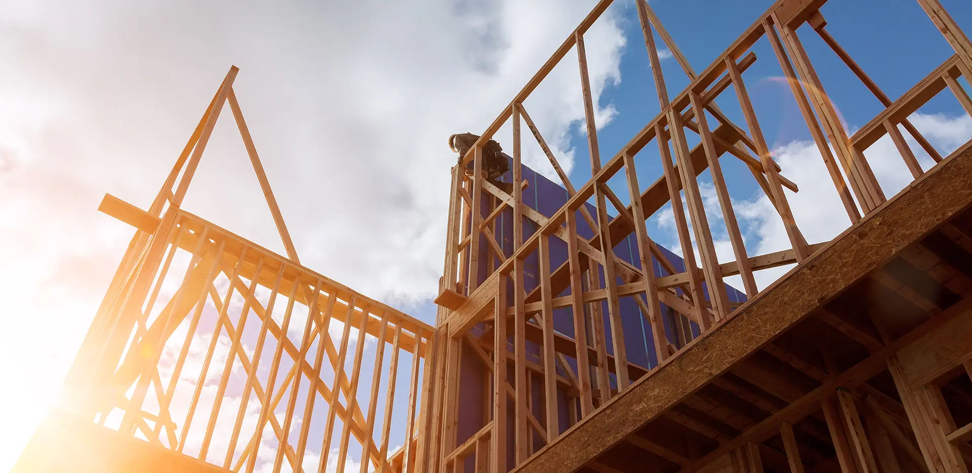 A worker climbing atop the framework of a house under construction.