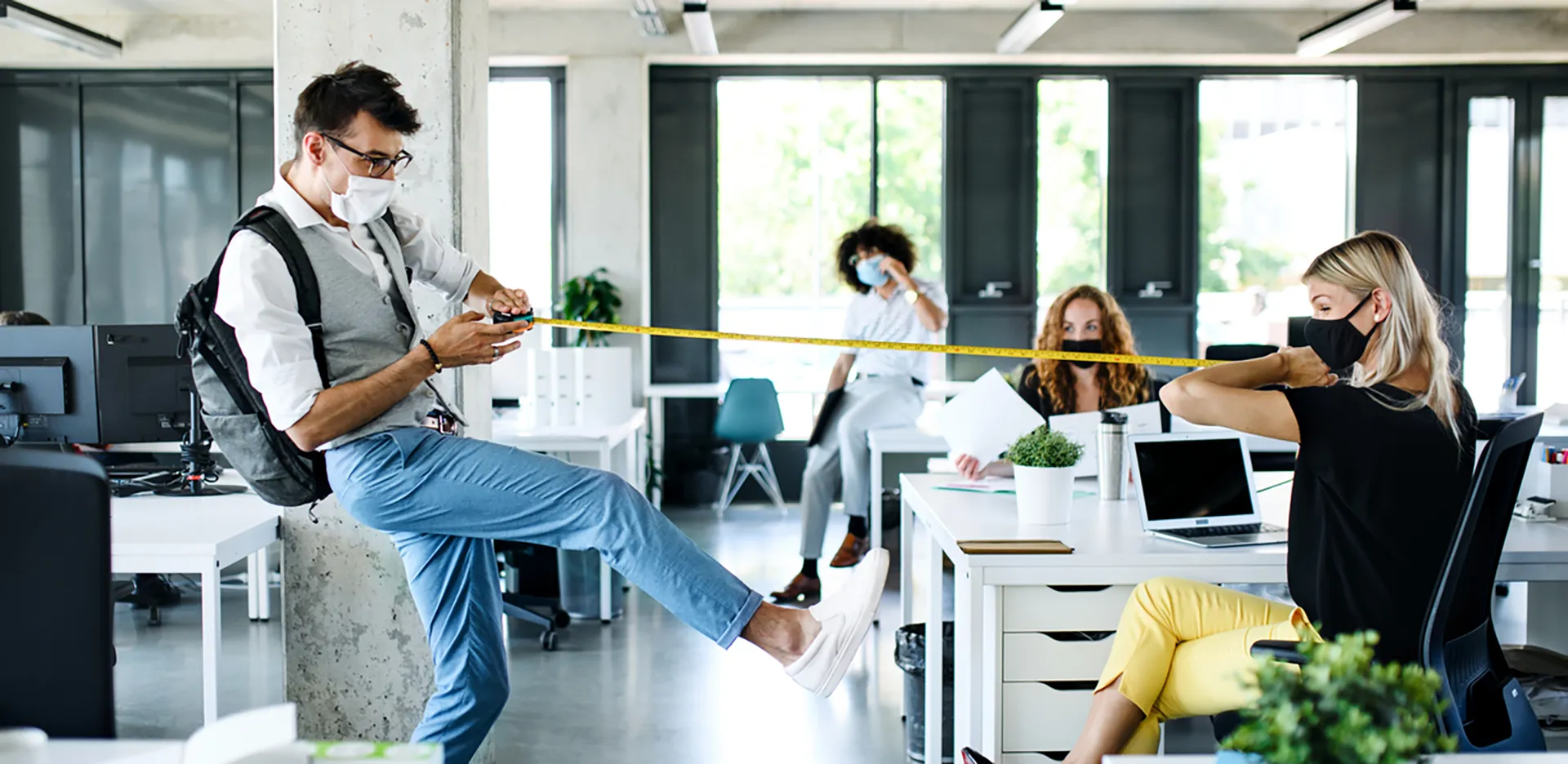 A pair of office workers wearing masks stretching a tape measure between them.