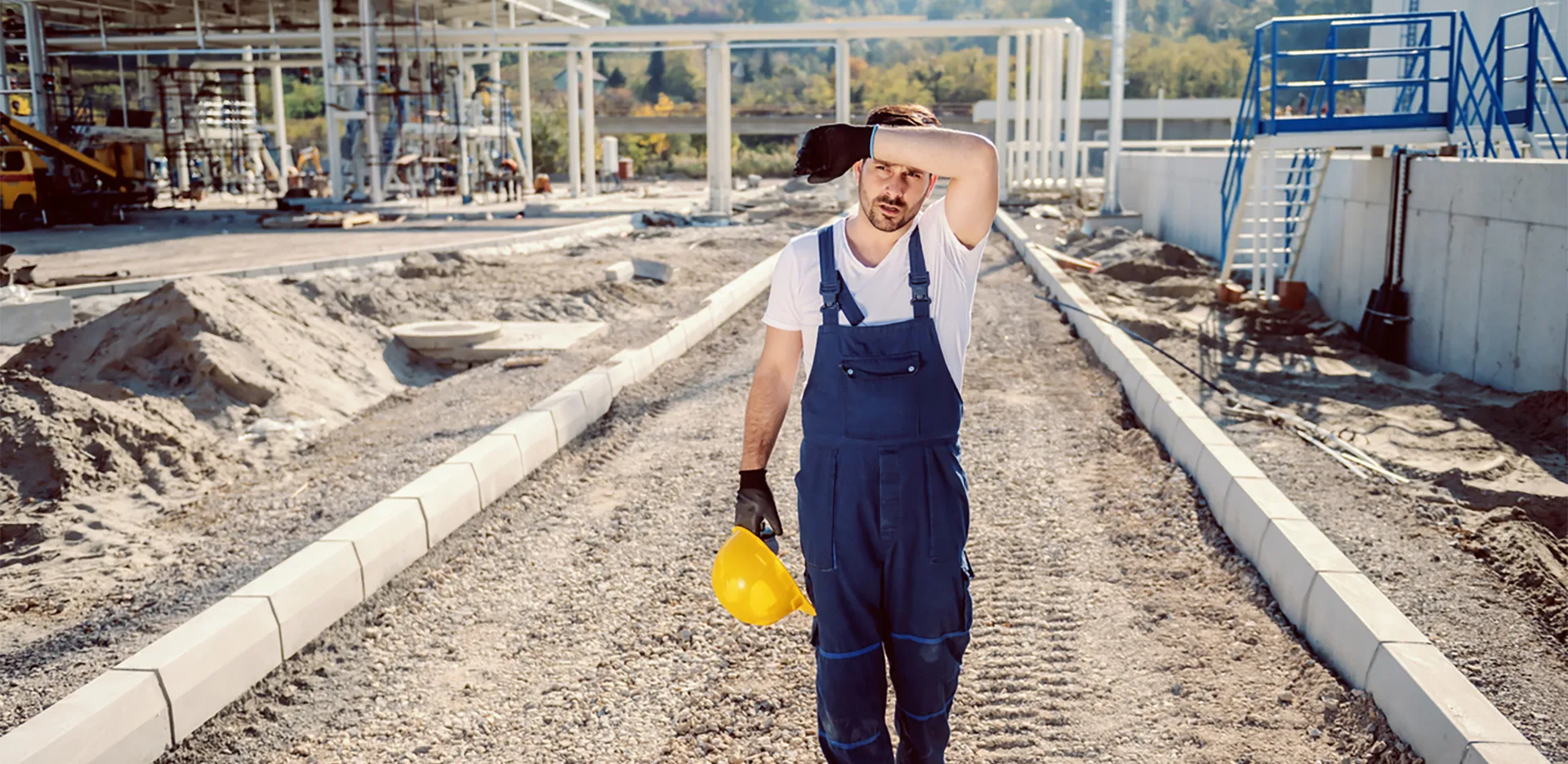 A construction worker on a job site wiping sweat off of their forehead.