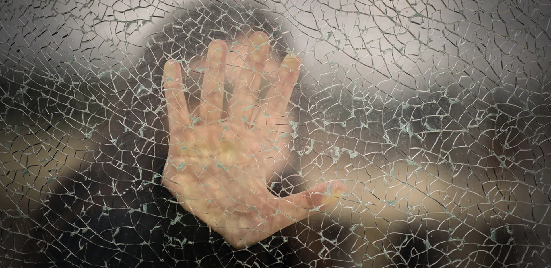 A hand against glass with cracks running through it.