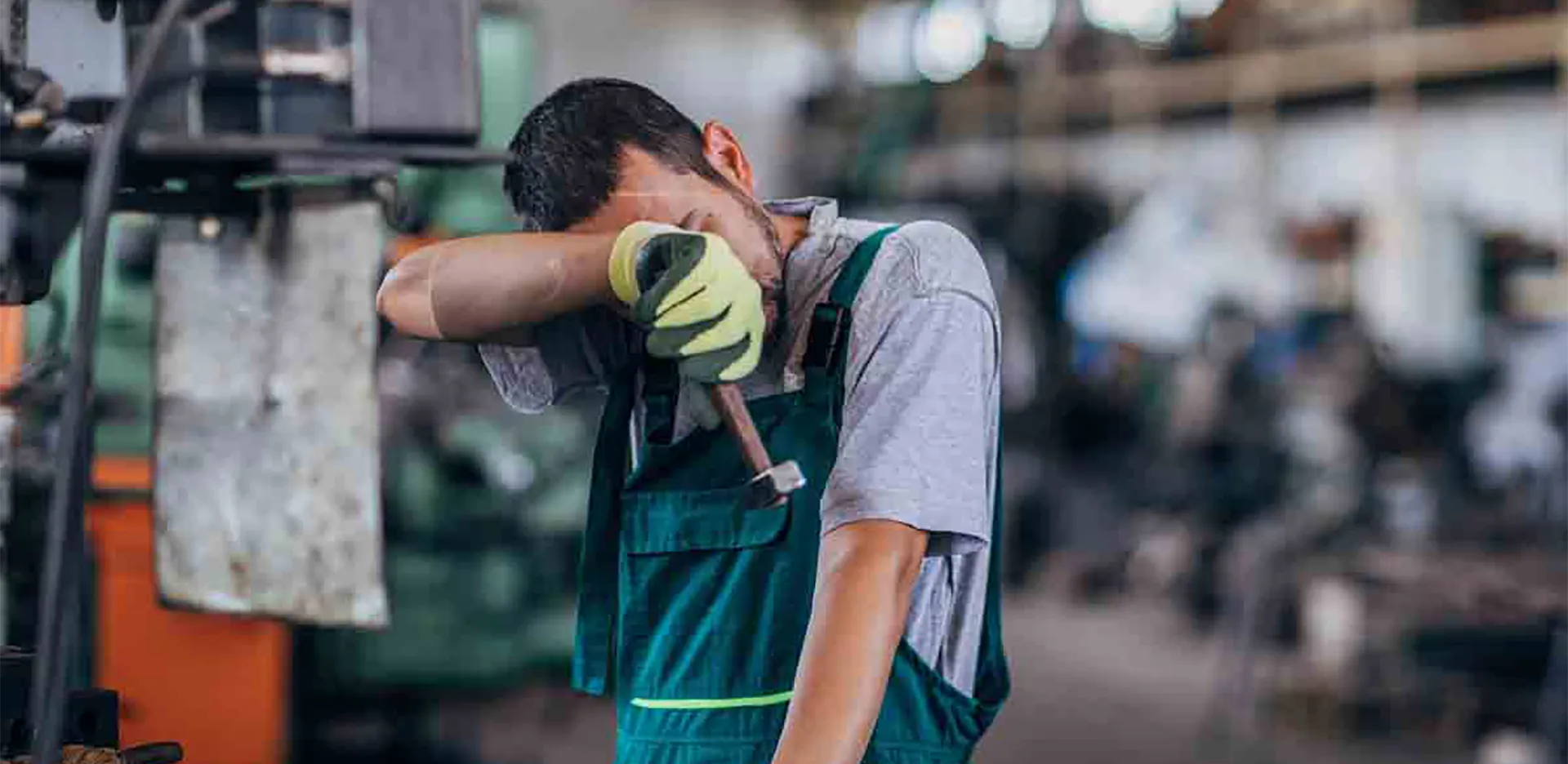 A worker wearing an apron and gloves wiping sweat off of their forehead.