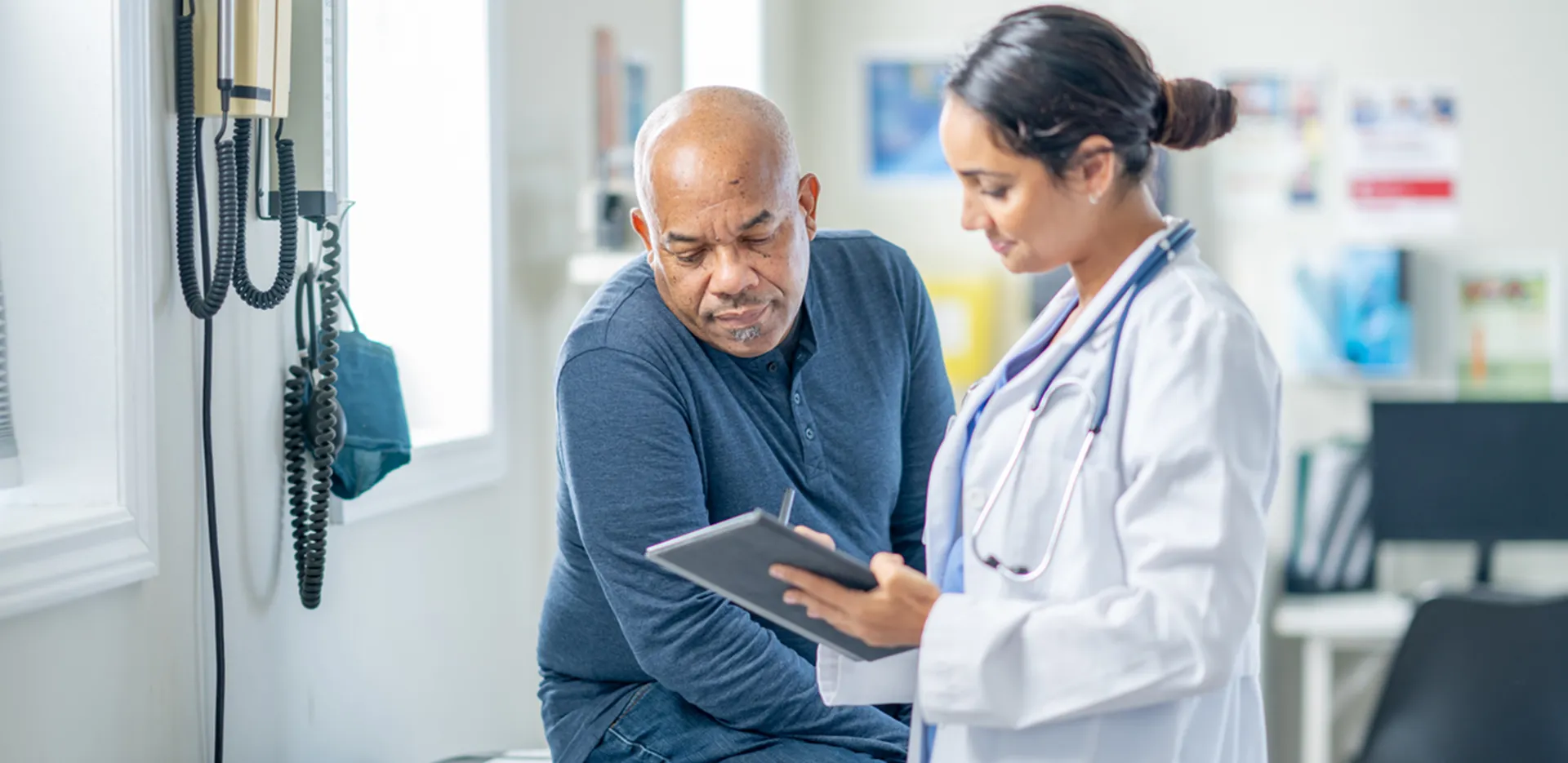 A doctor and patient looking over a tablet while in an examination room.