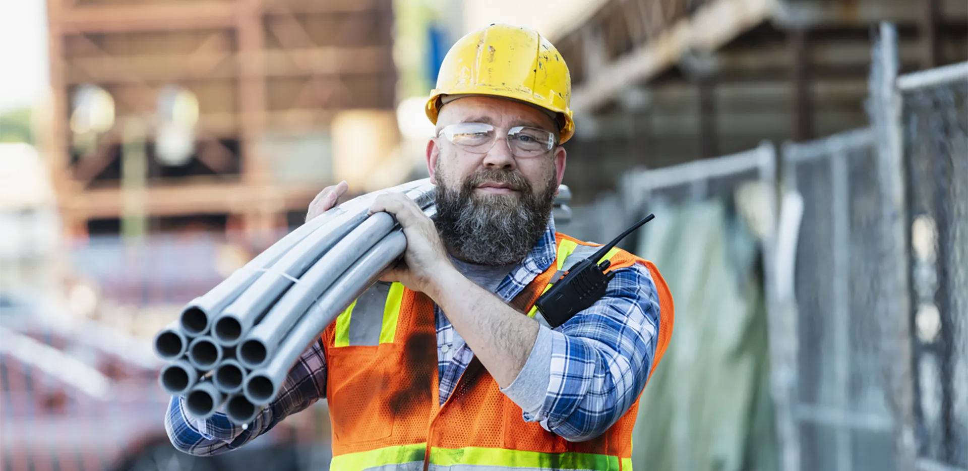 A construction worker carrying a bundle of PVC pipes.
