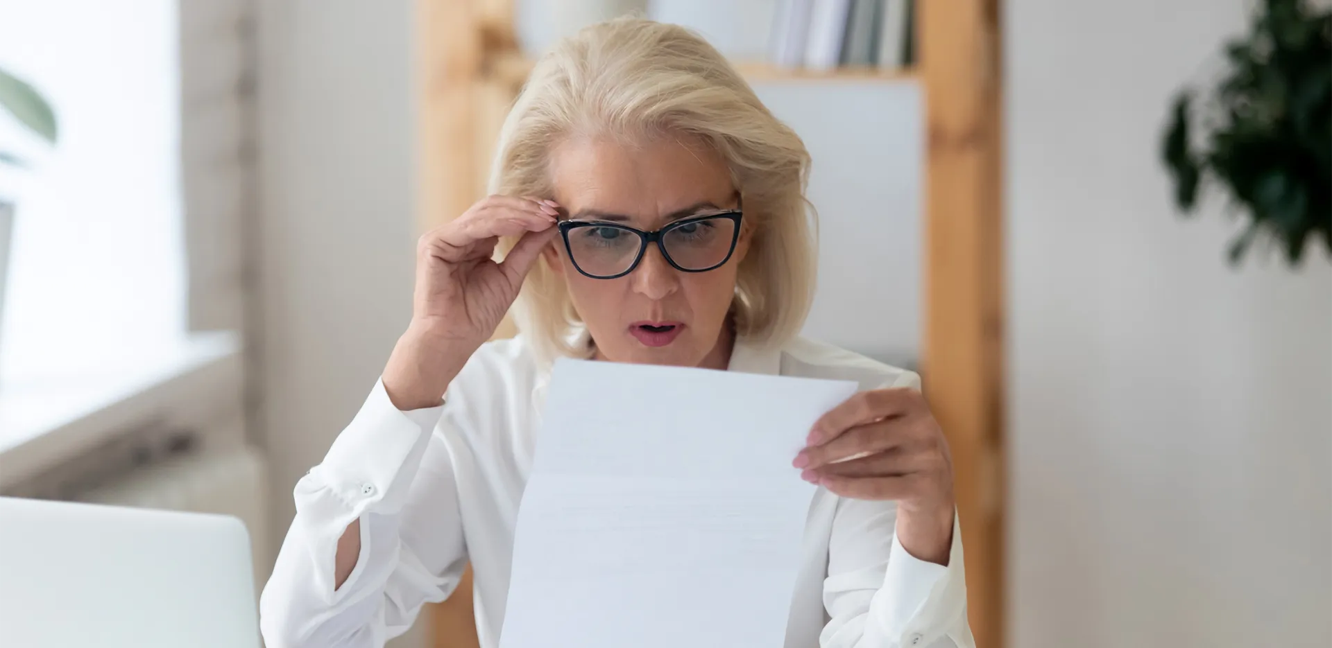 A woman looking at a piece of paper looking shocked.