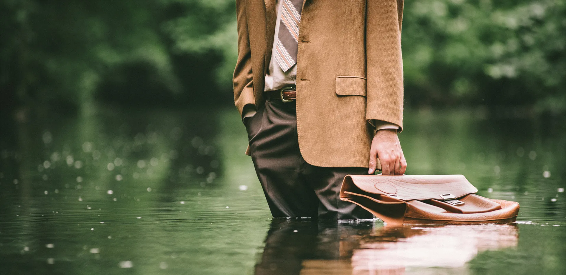 A business person standing in water up to their knees, with their briefcase by their side.