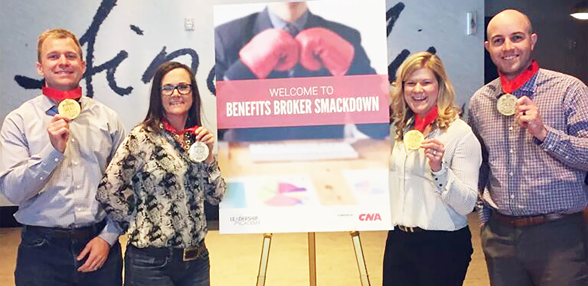 InterWest team members holding up gold medals in front of a sign reading 'Welcome to Benefits Broker Smackdown.'