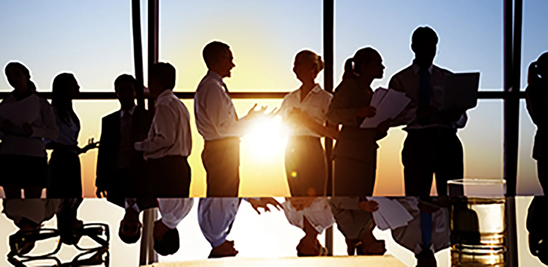 Business people talking next to a conference table in front of a large window.