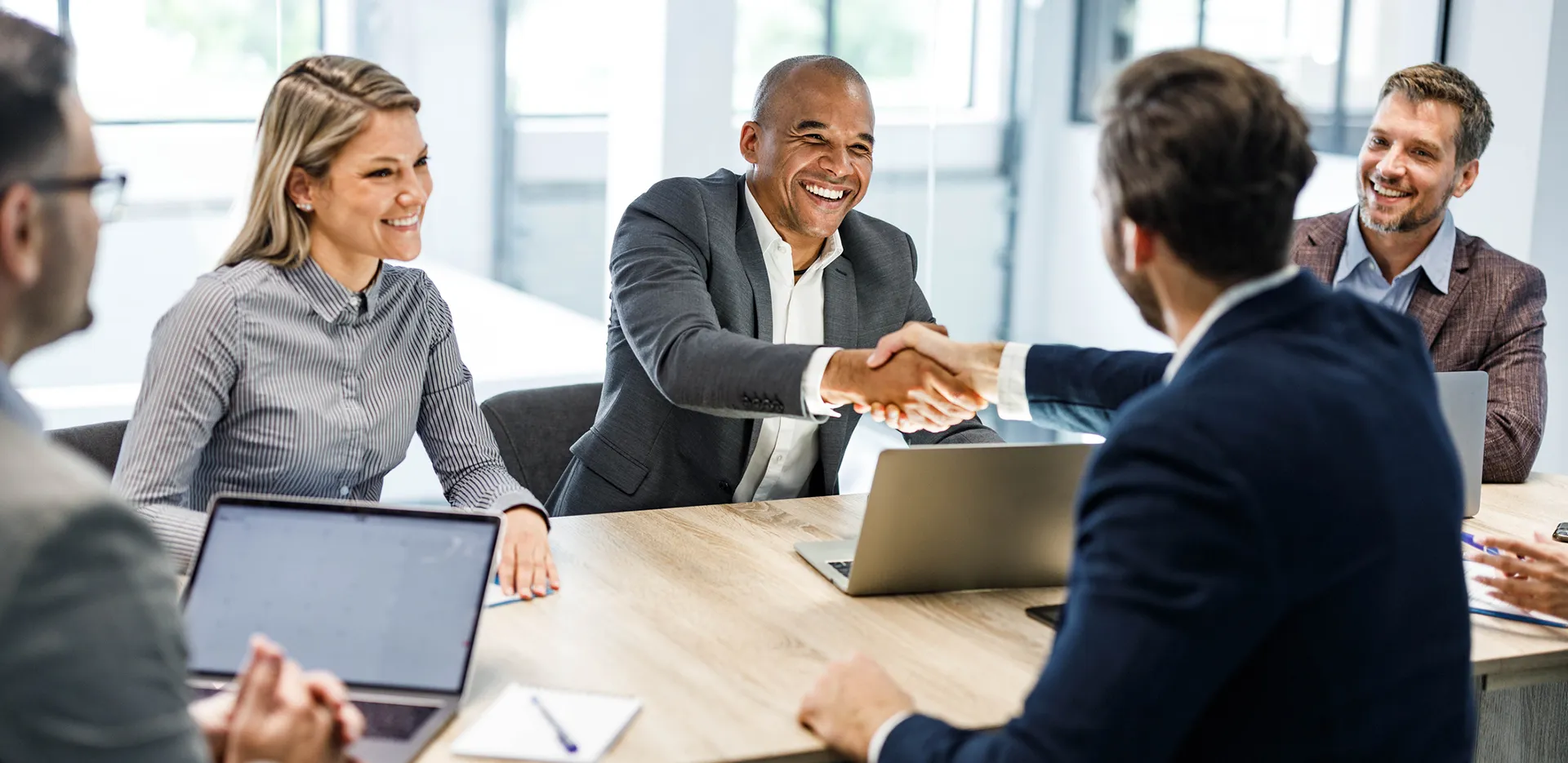 Two businessmen shaking hands while their colleagues look on.