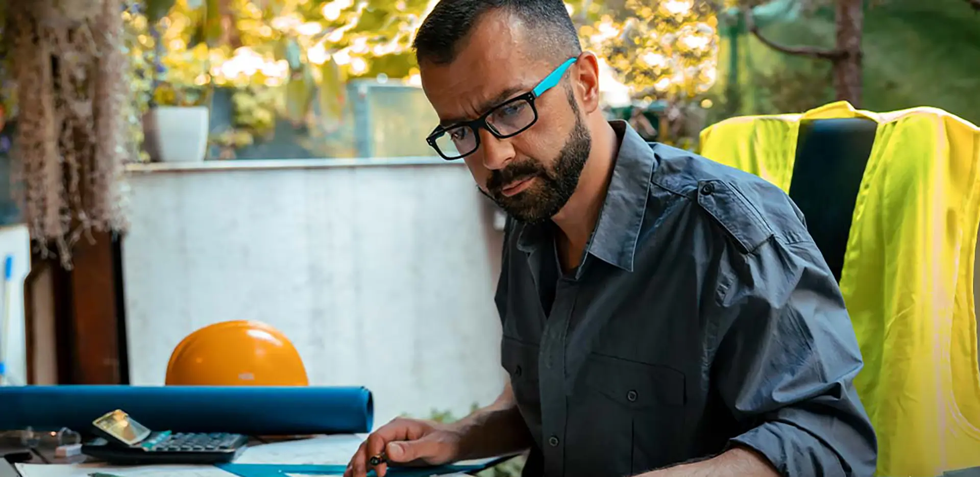 A contractor looking seriously at a table with blueprints, a calculator, and other tools.