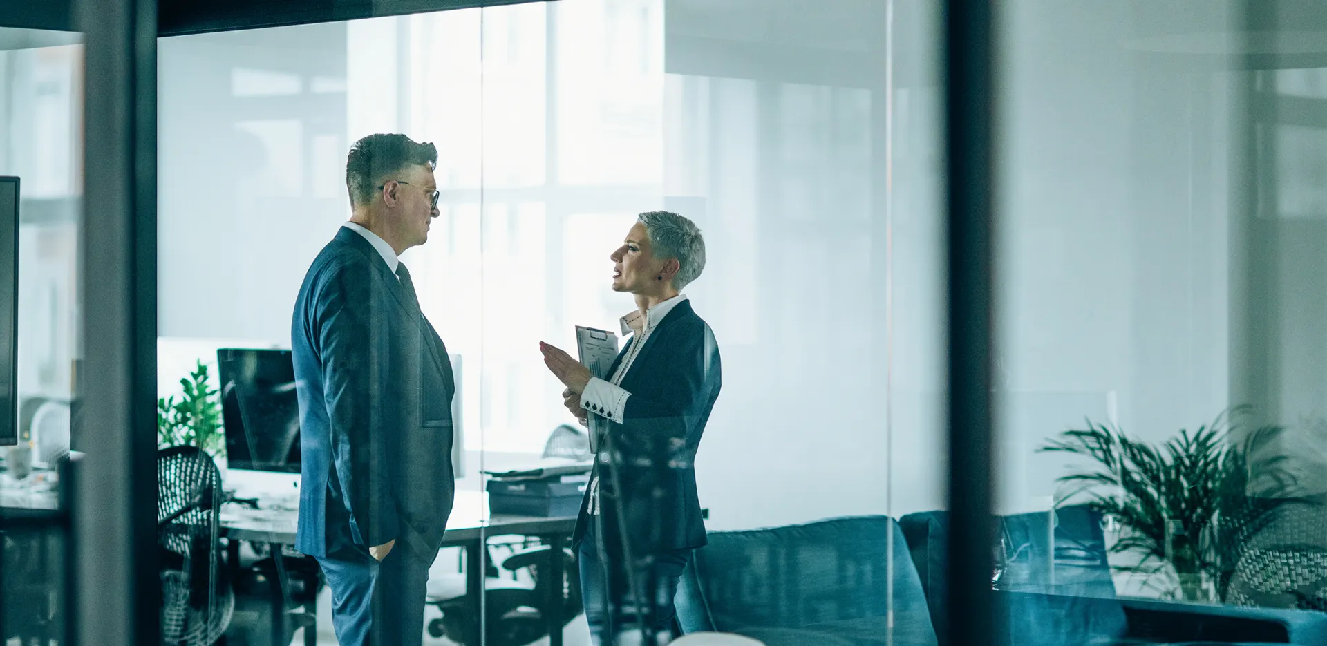 Two business people wearing suits speak in an office building.