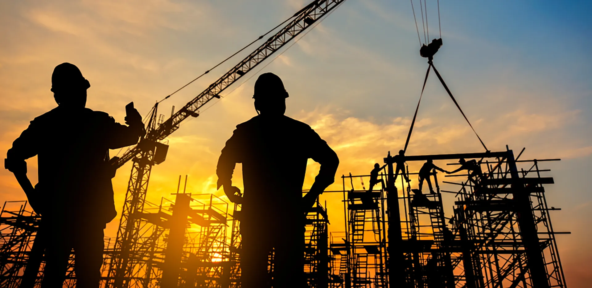 Silhouettes of construction workers on scaffolding at sunset.