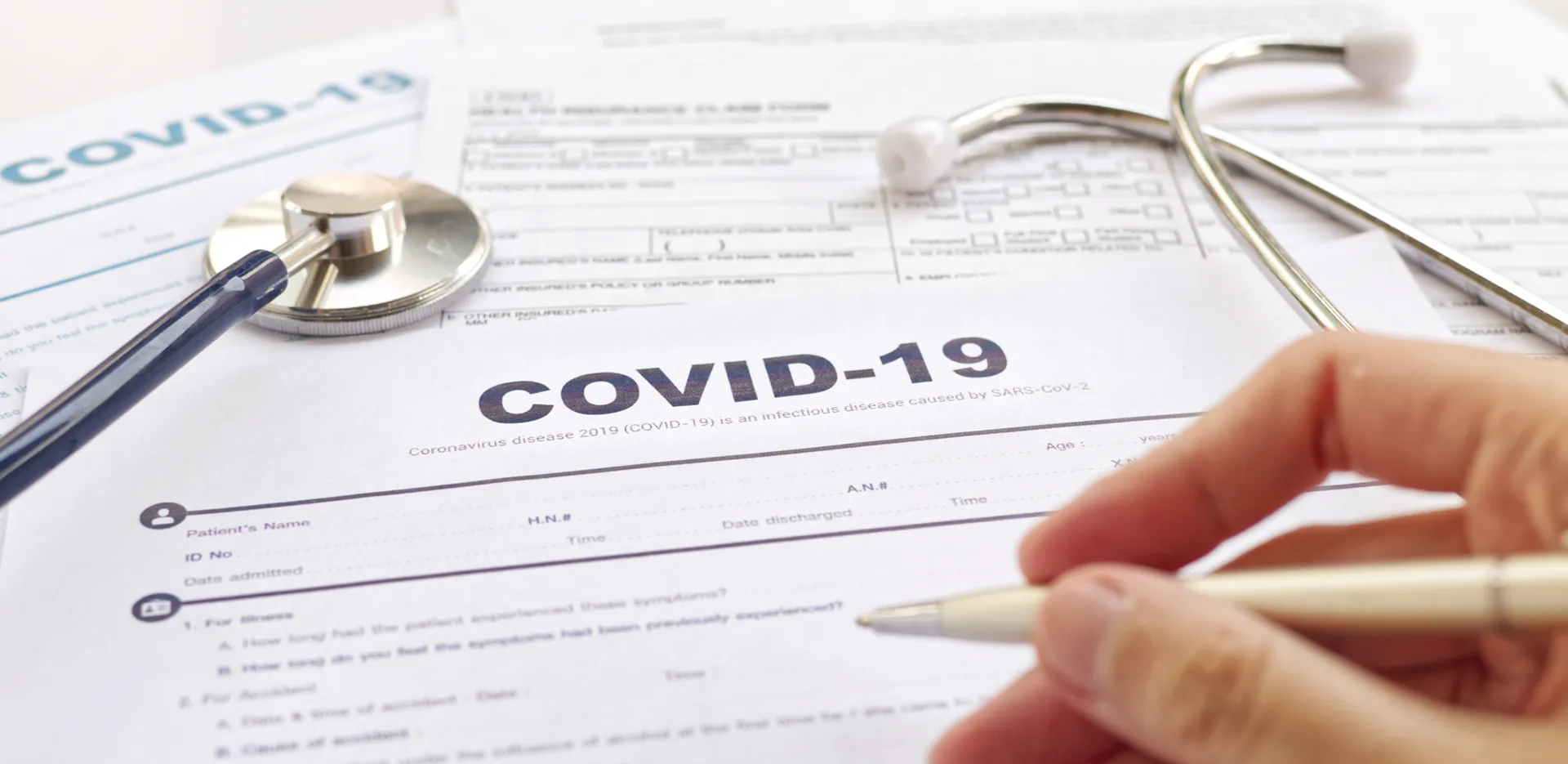A hand signing paperwork that reads 'COVID-19' at the top.