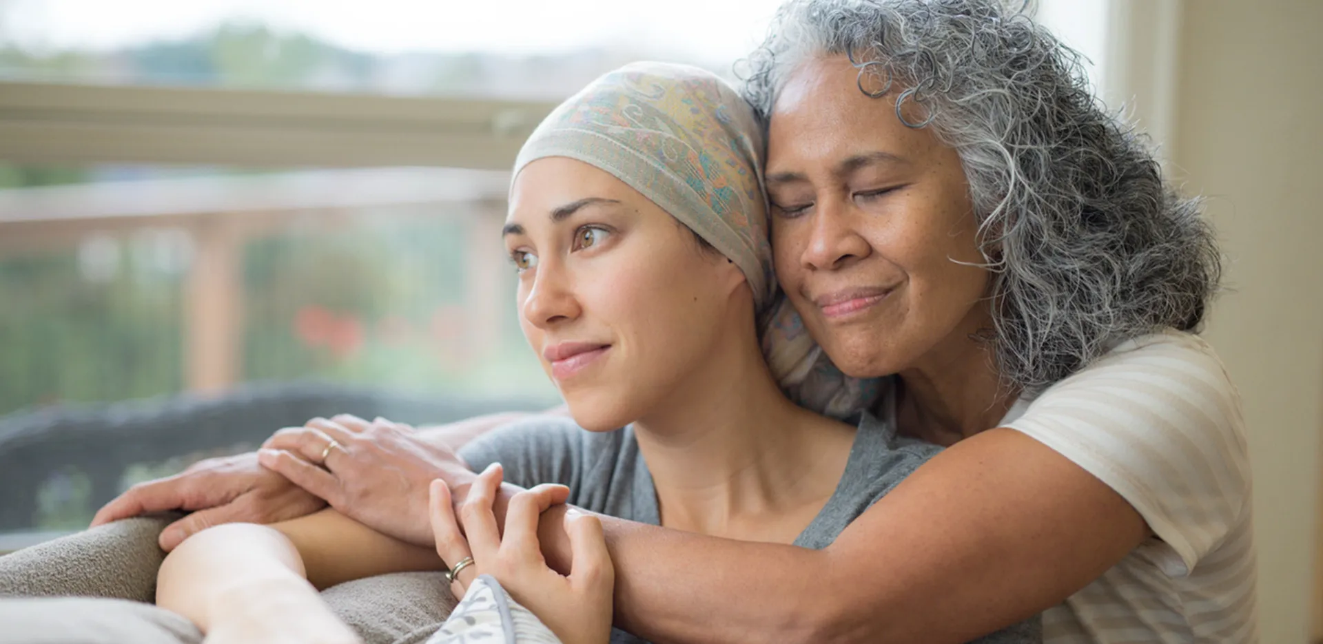 Two women embracing on a couch, one with a handkerchief tied over her head.