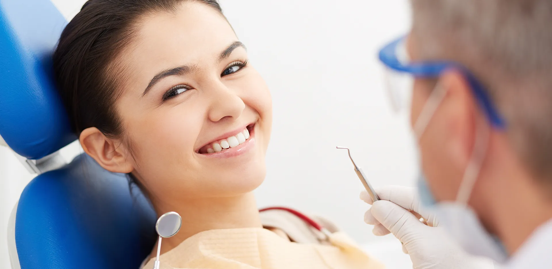 A young woman in a dentist's examination chair smiling at the camera.
