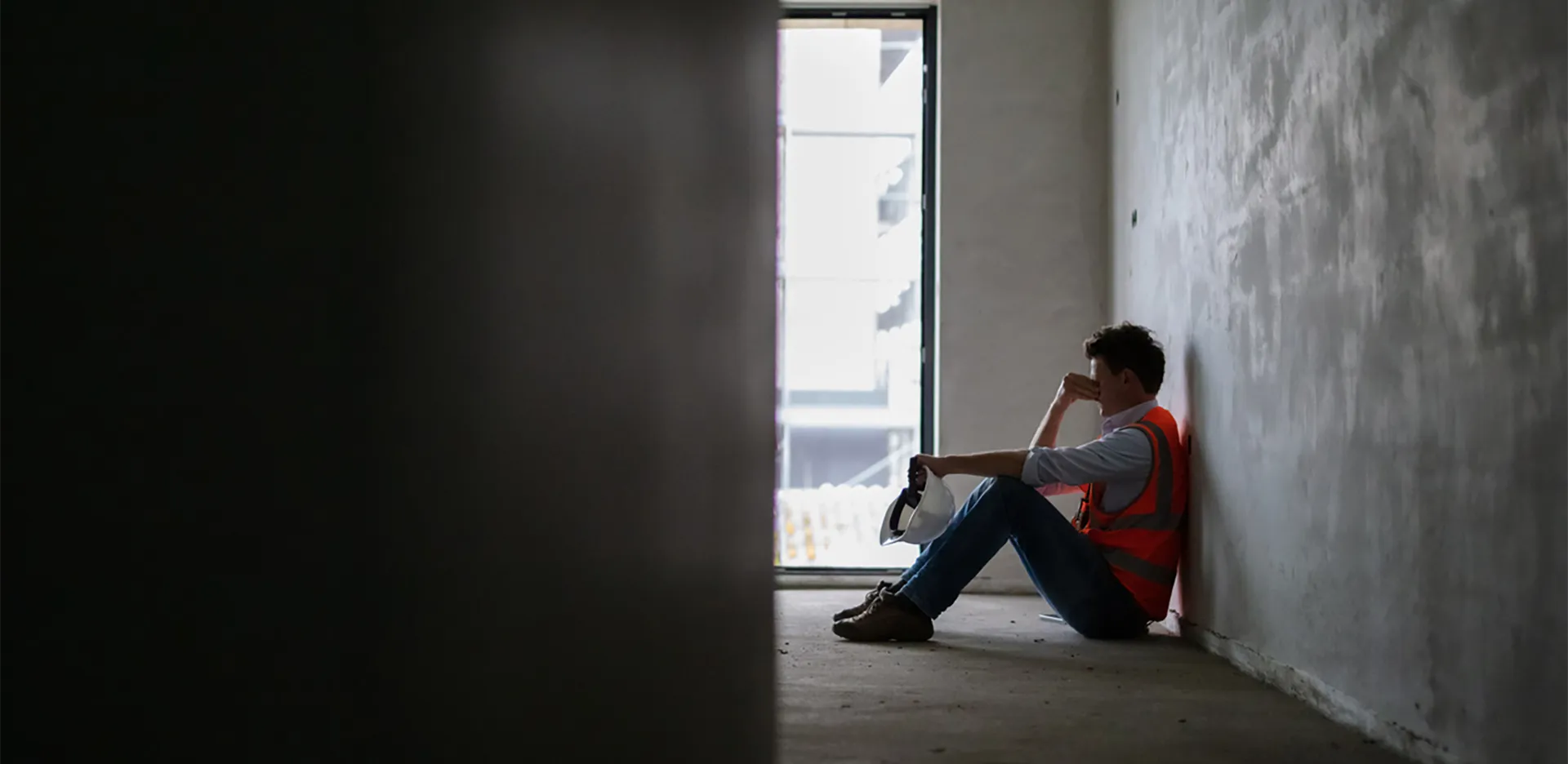 A construction worker sitting on the ground rubbing their forehead.