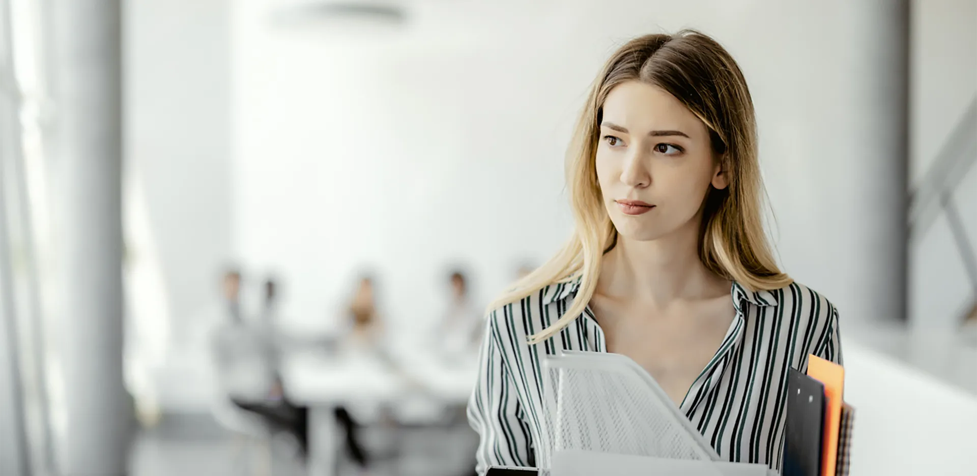 A professionally dressed woman carrying a box of supplies from her desk.