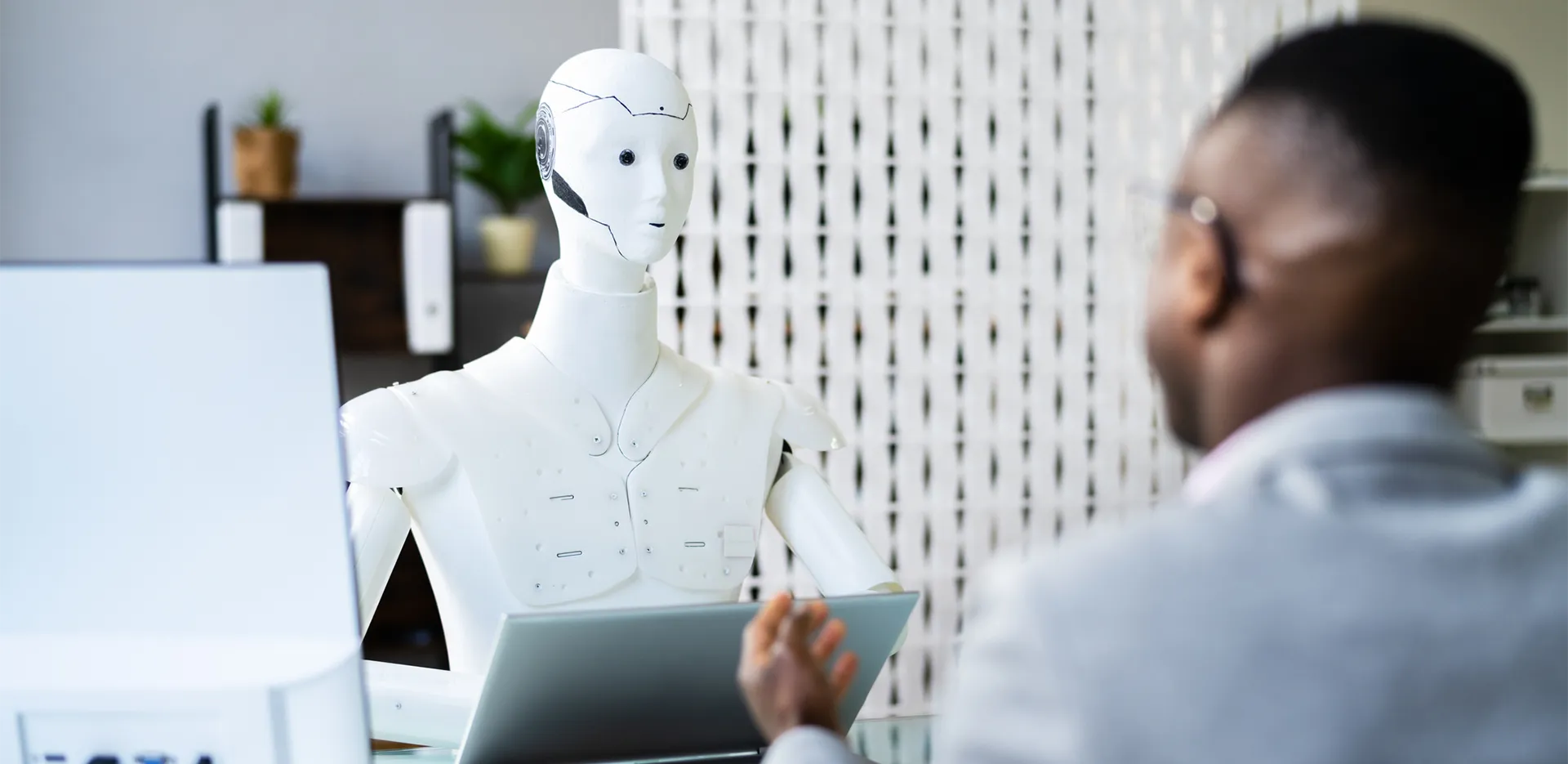 A robot sitting at a laptop speaks with a job candidate.